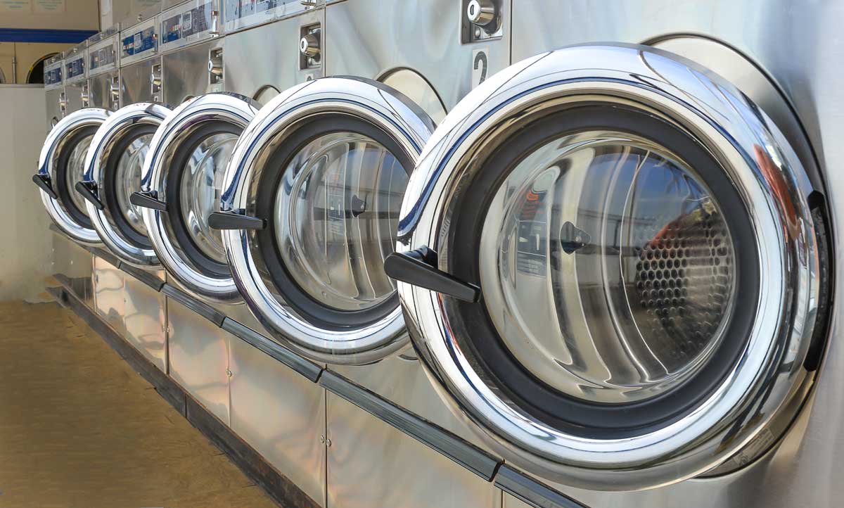 Row of industrial laundry machines in laundromat.
