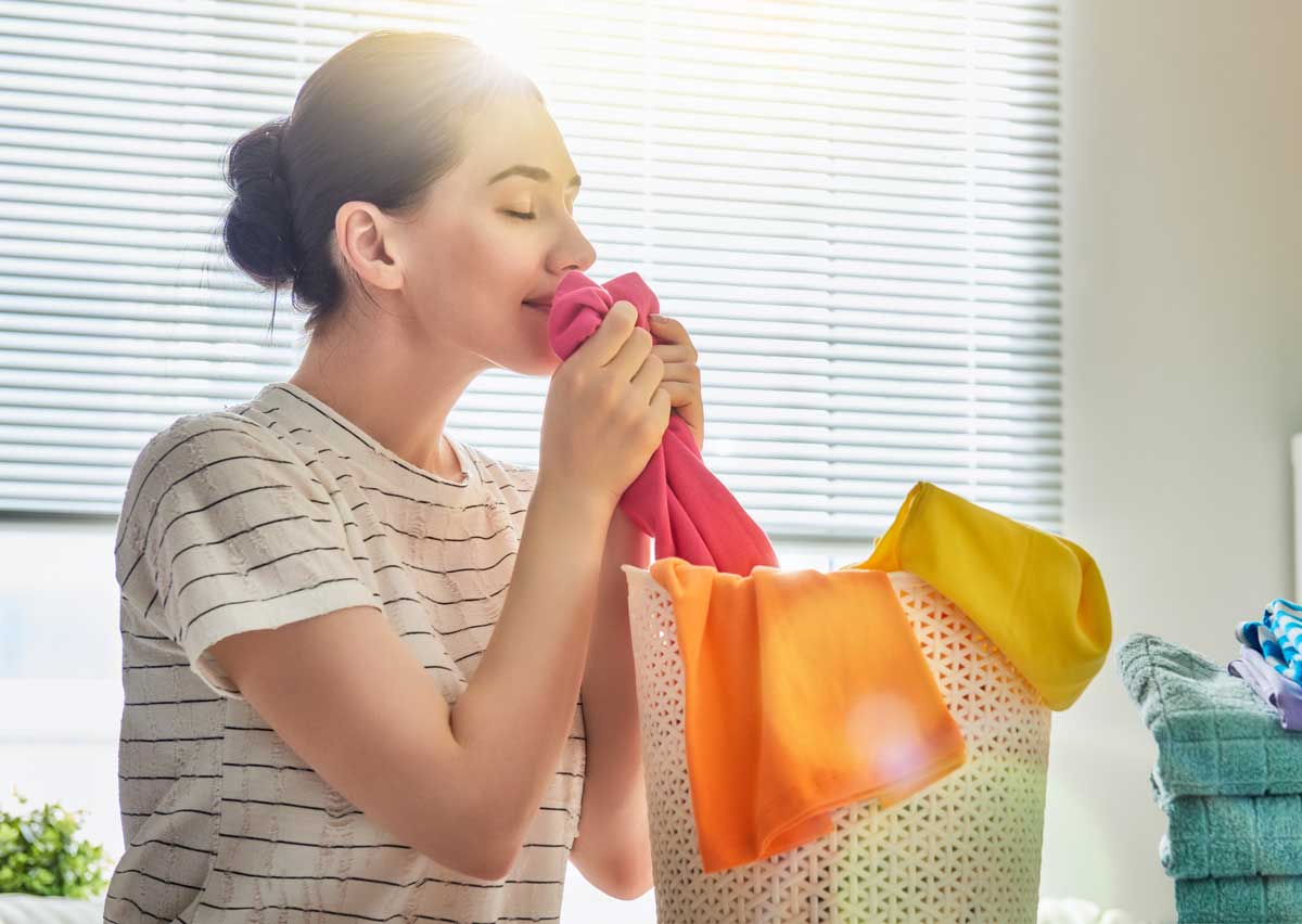 Beautiful young woman is smelling clean clothes and smiling while doing laundry at home.