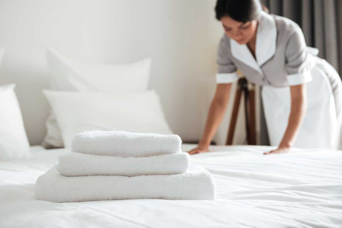 Young hotel maid making the bed with clean fresh towels