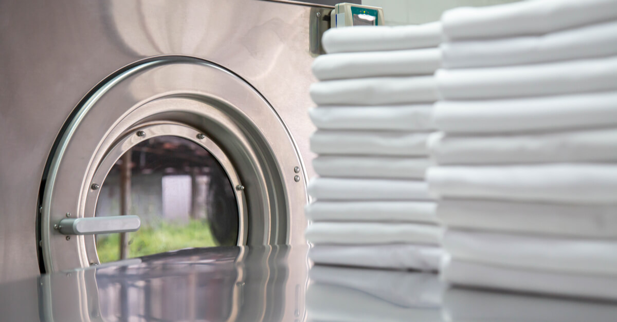 Stack of clean bed sheets in front of industrial washing machine. Focused on washing machines. washing machine eco friendly